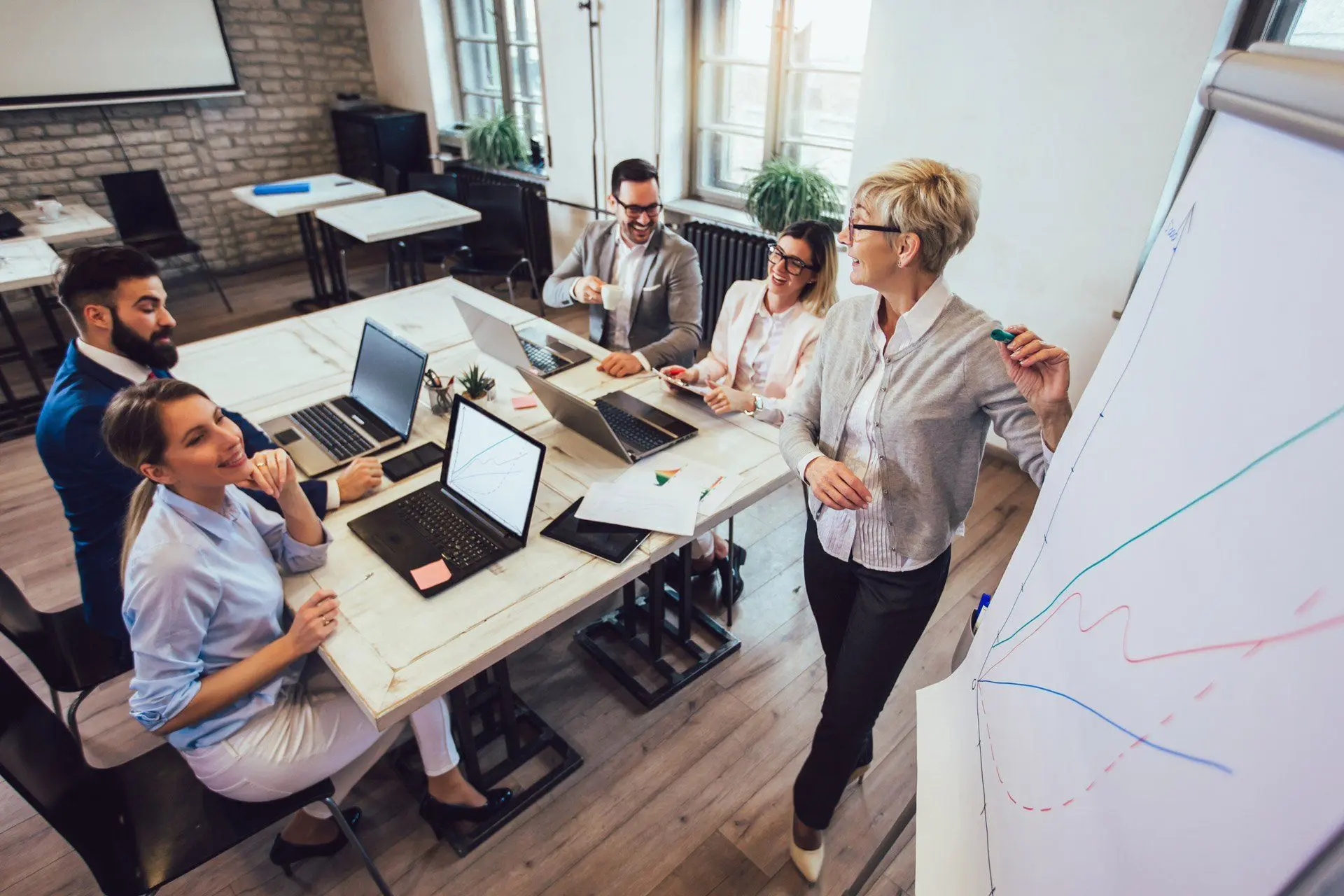 Team meeting around a table while a colleague explains a chart on a whiteboard